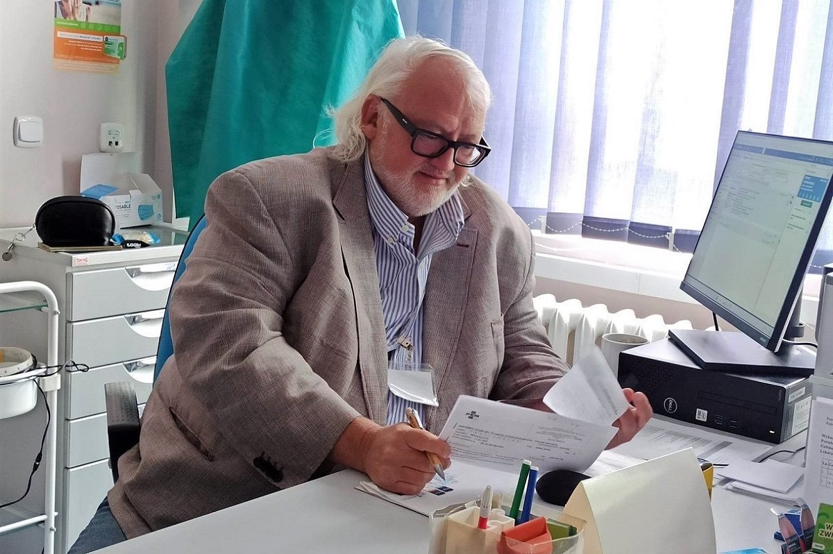 Profesor Biliński przy biurku w gabinecie przegląda dokumentację medyczną